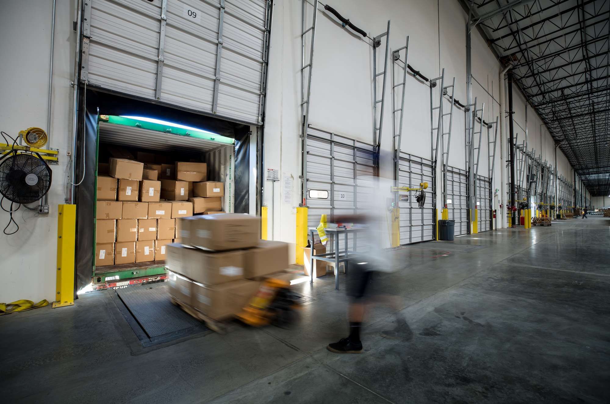A blurred worker moves boxes off a semi-truck to a warehouse.