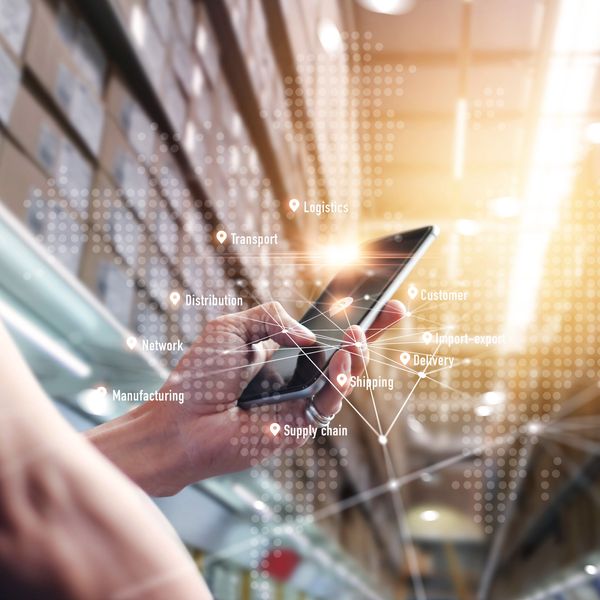 A hand holds a cell phone with a warehouse backdrop.