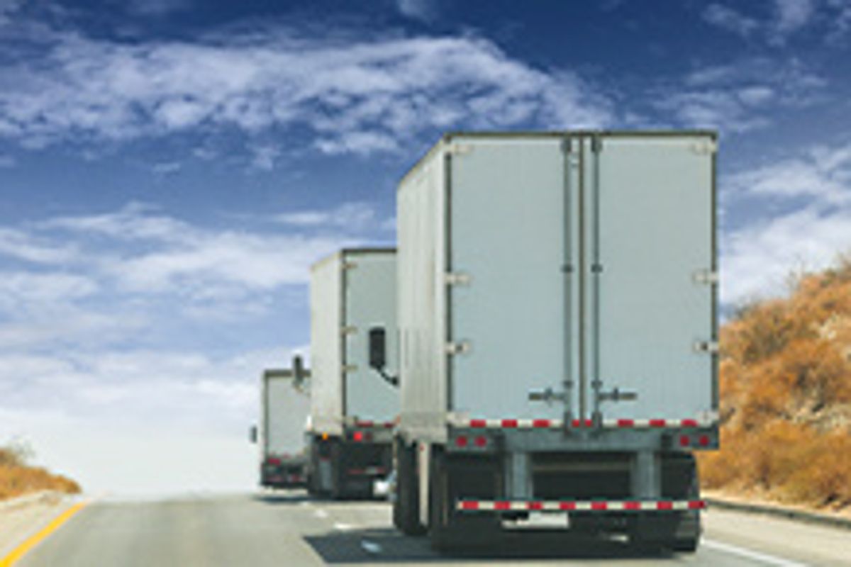 A line of box trucks drive up the road.