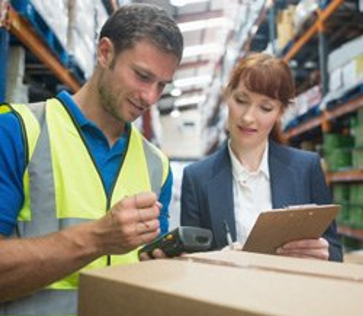 A man and a women review the delivery of a package while standing in a warehouse.