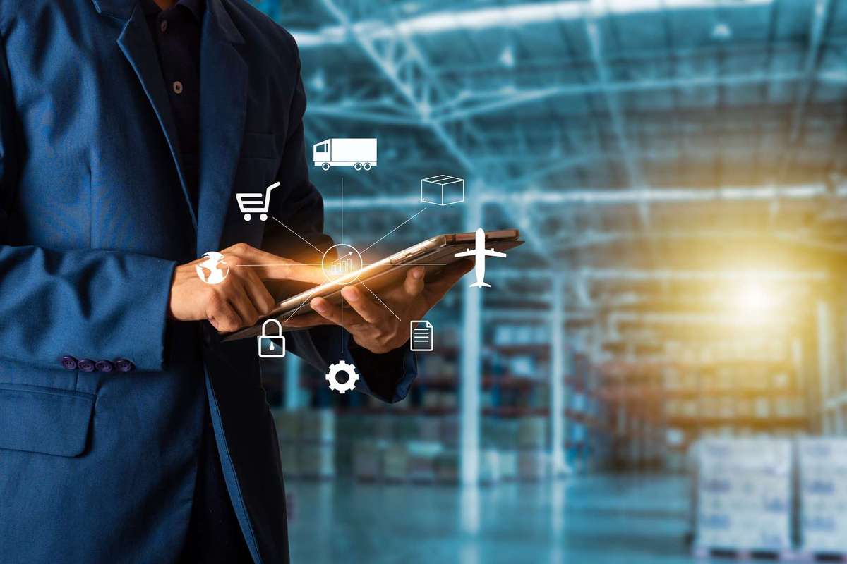 A man in a dark blue suit in a warehouse looks at a tablet device with a supply chain graphic overlayed on top.