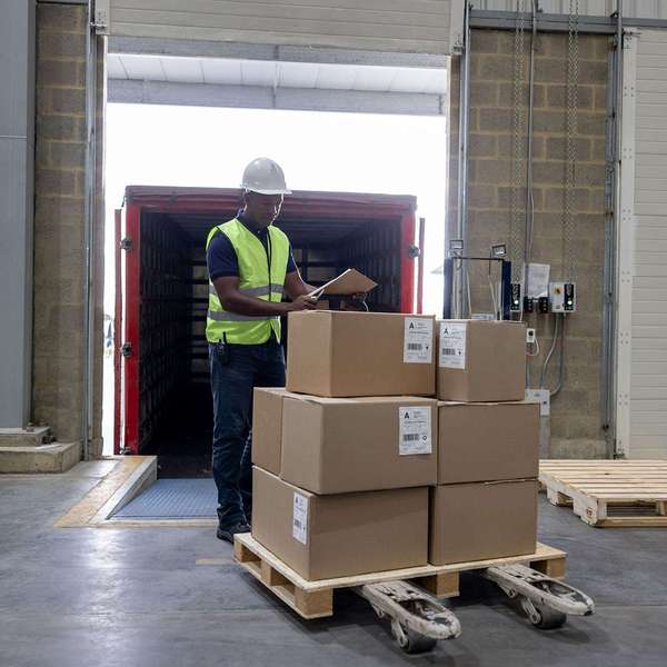 A man stands by a pallet of boxes on a forklift.