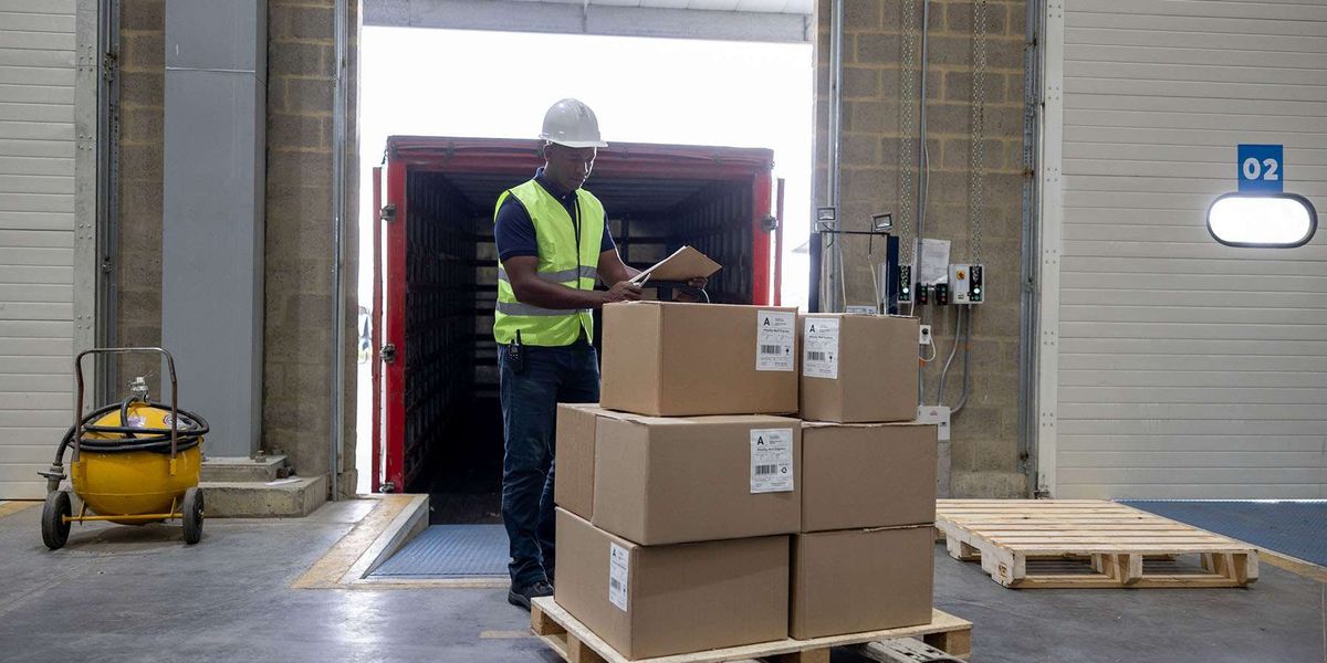 A man stands by a pallet of boxes on a forklift.