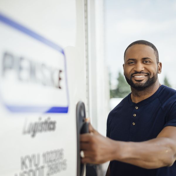 A Penske freight brokerage driver smiles at the camera as he opens the door to his Penske truck.