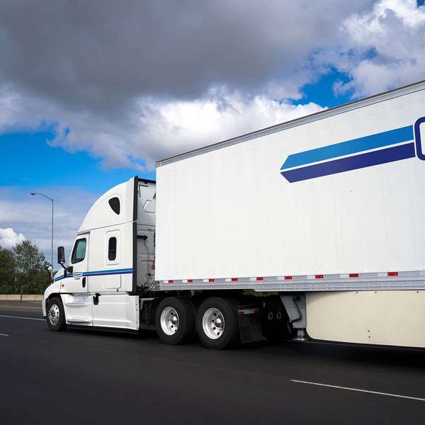 A photo from the side of a white and blue Penske Logistics semi-truck driving on the road.