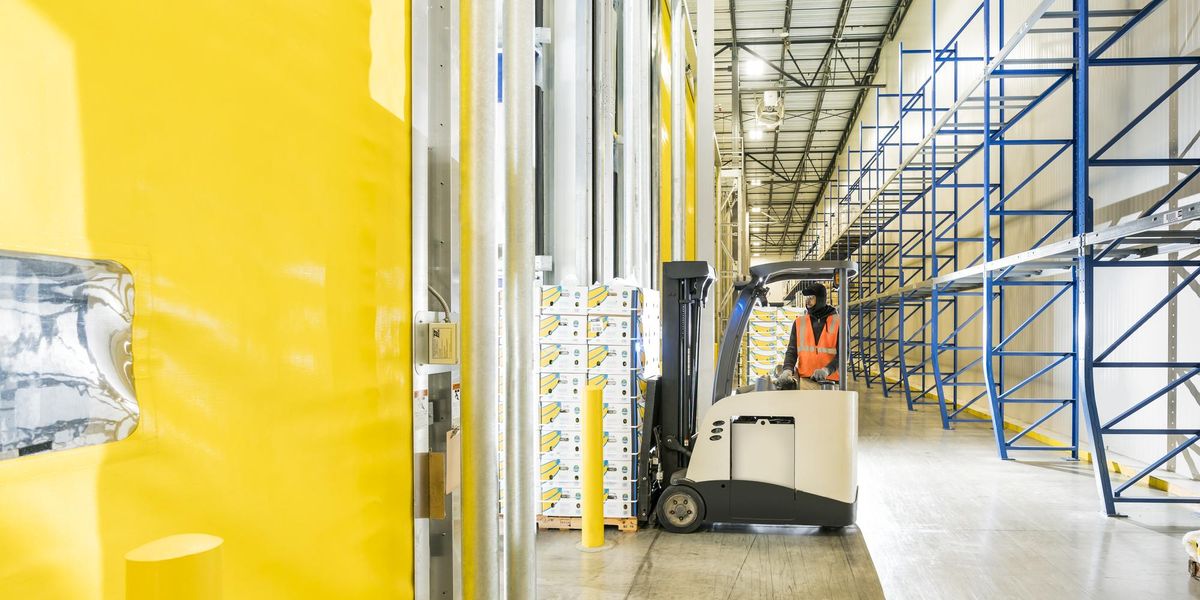 a sustainable warehouses uses natural light from skylights while a worker uses a forklift.