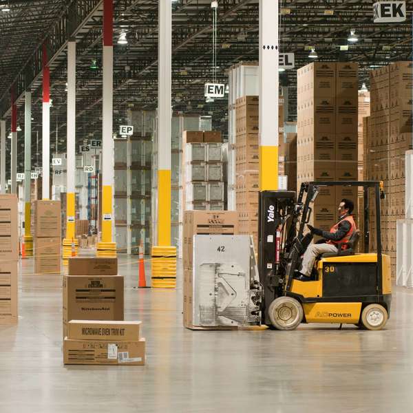 A warehouse worker moves boxes with a forklift inside a warehouse.