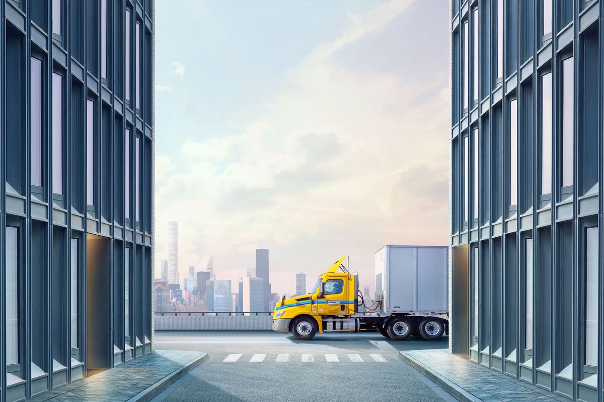A yellow and white Penske semi-truck drives along a city road.