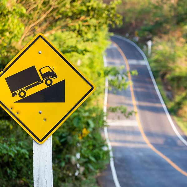 An increased incline road sign next to a road hill.