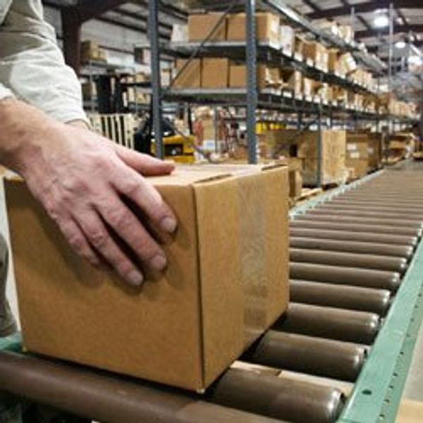 Close up of hands pushing a brown box down a conveyor belt.