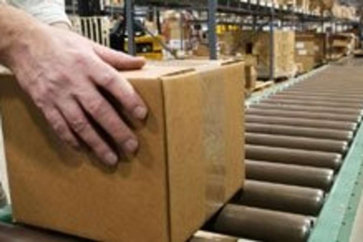 Close up of hands pushing a brown box down a conveyor belt.