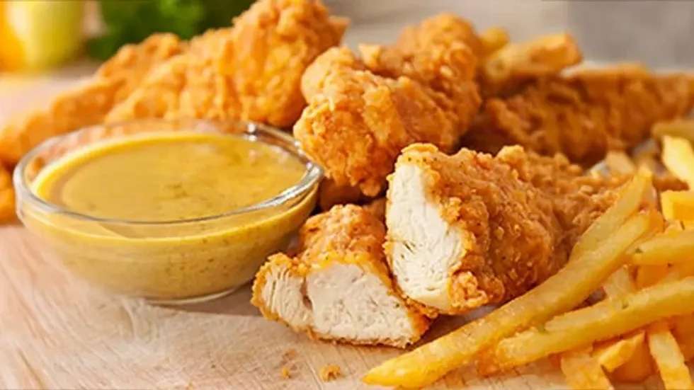 Crispy chicken tenders with fries and dipping sauce on a wooden surface.
