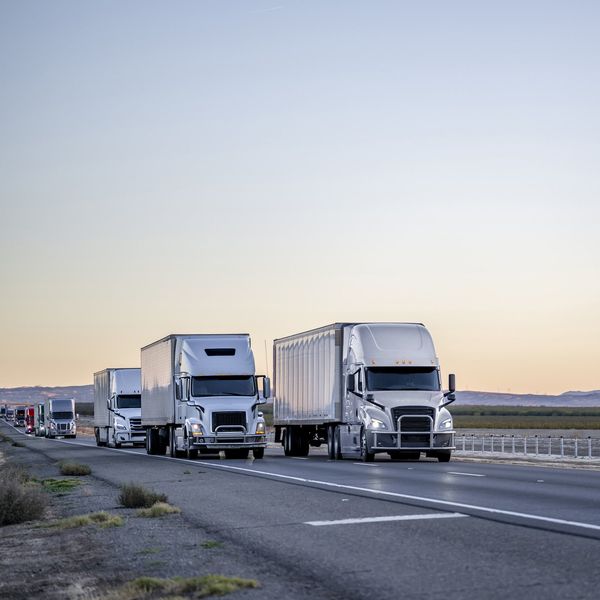 Multiple semi-trucks drive up a road.