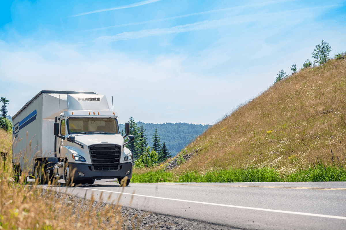 Penske Logistics tractor-trailer driving in springtime scenery.