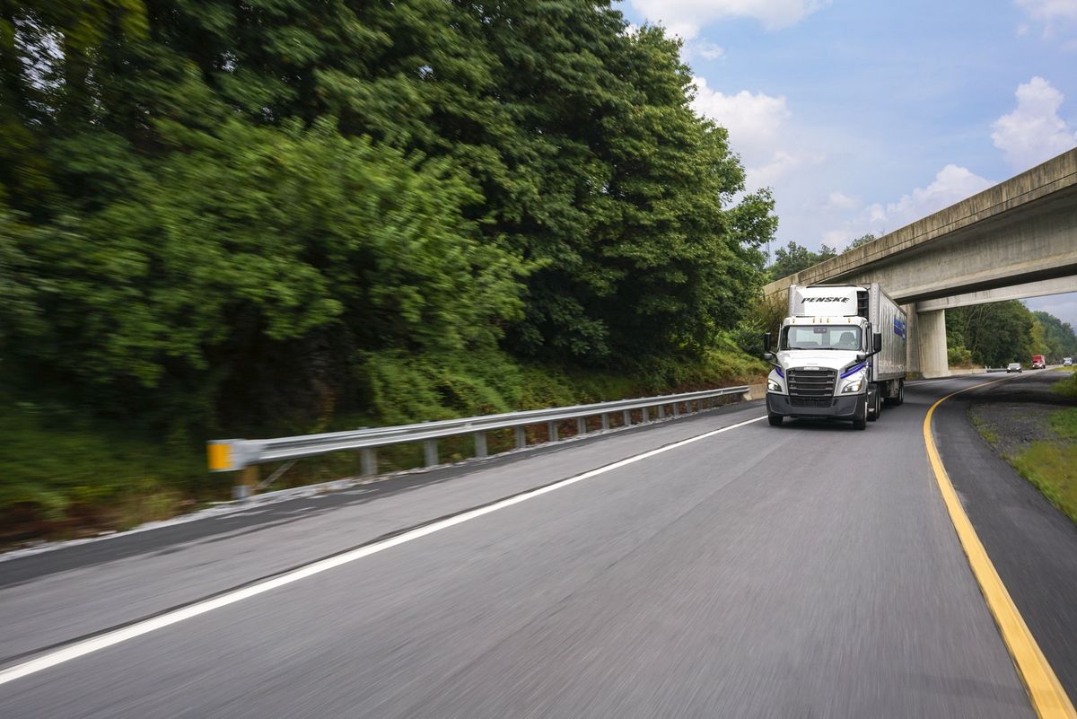 Penske Logistics Truck driving on highway with trees