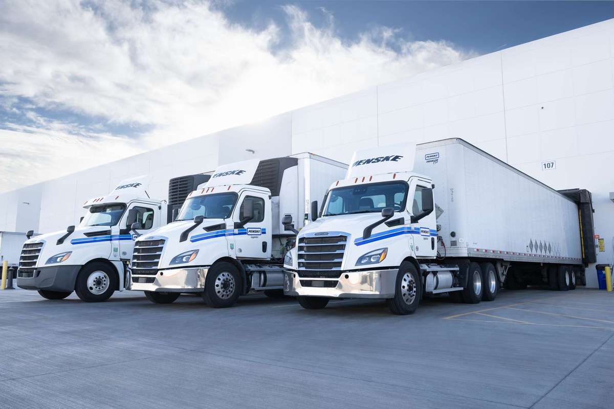 Three Penske trucks lined up at a warehouse dock.