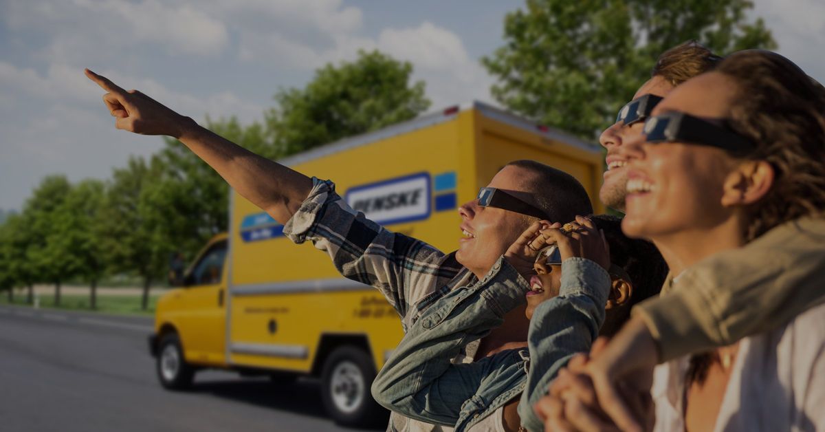 Three people wearing solar eclipse glasses watch the eclipse.