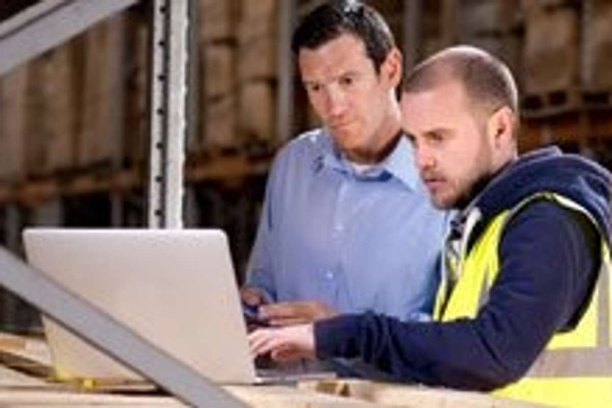 Two men looking at a laptop while in a warehouse.