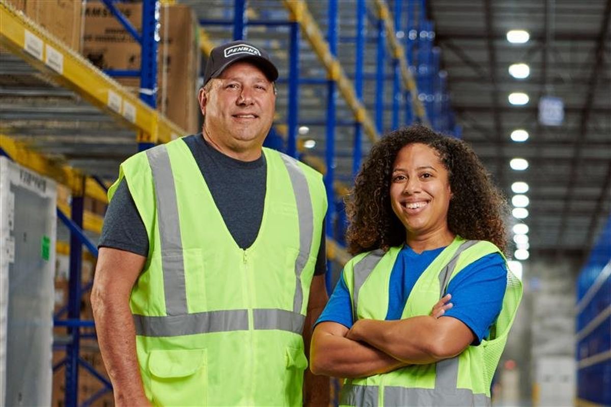 Two Penske warehouse associates stand in a distribution center aisle, showcasing teamwork and professionalism during Warehouse Associate Appreciation Week.