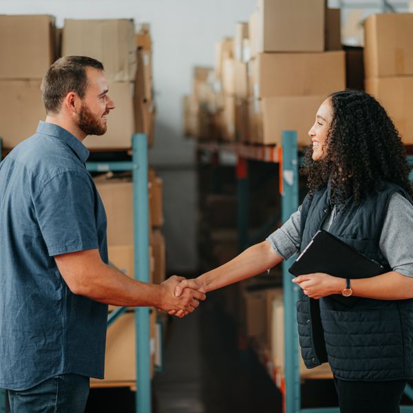 Two professionals shake hands in a warehouse setting.