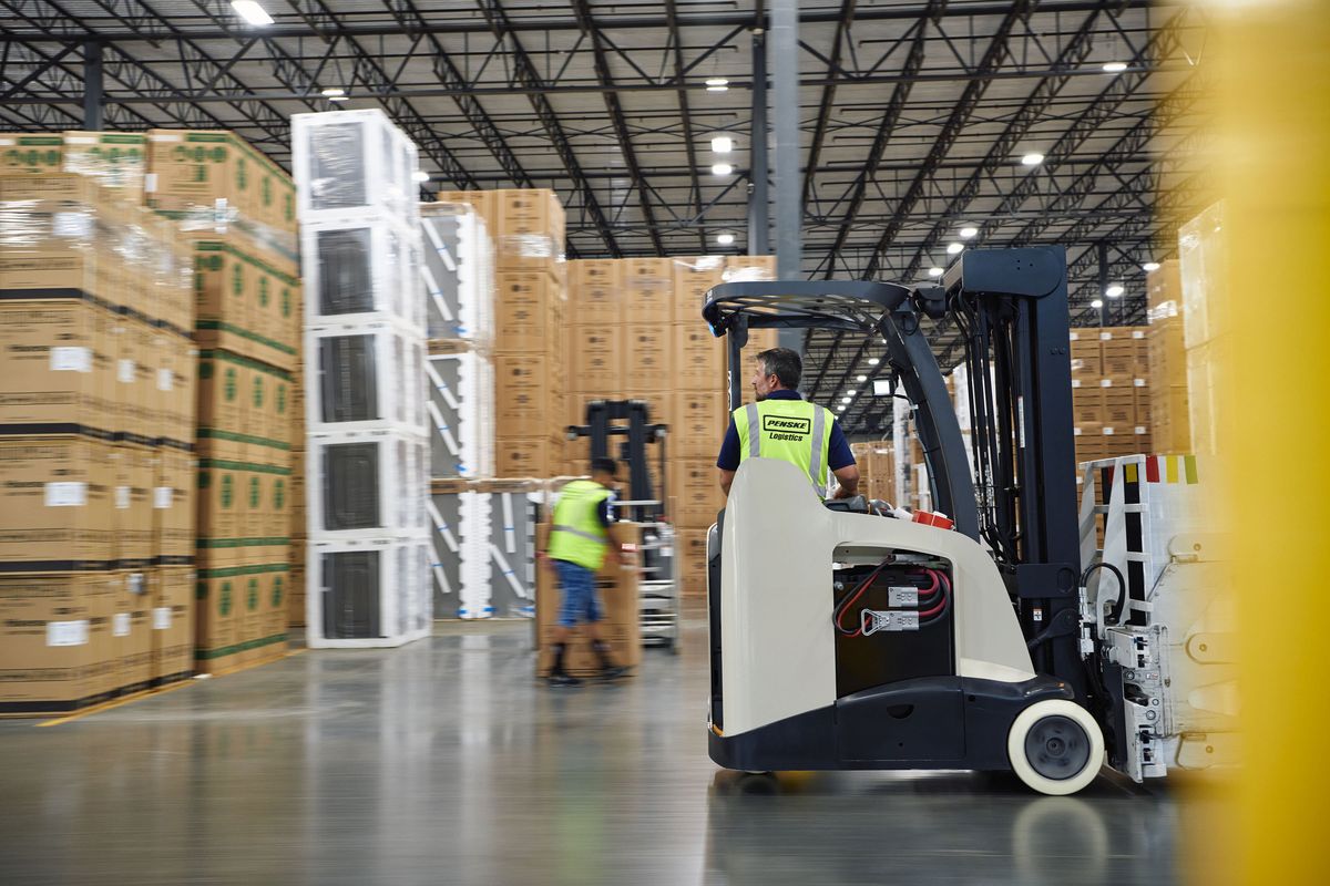 Two warehouse workers move boxes in a warehouse.