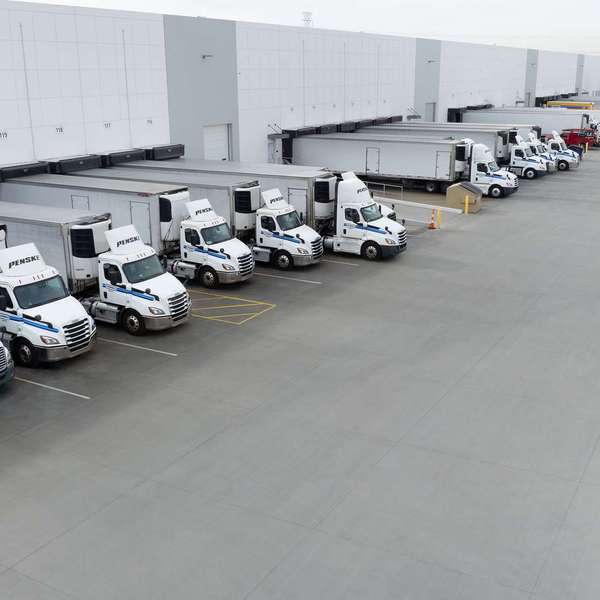 White Penske semi-trucks backed up to a warehouse loading dock.
